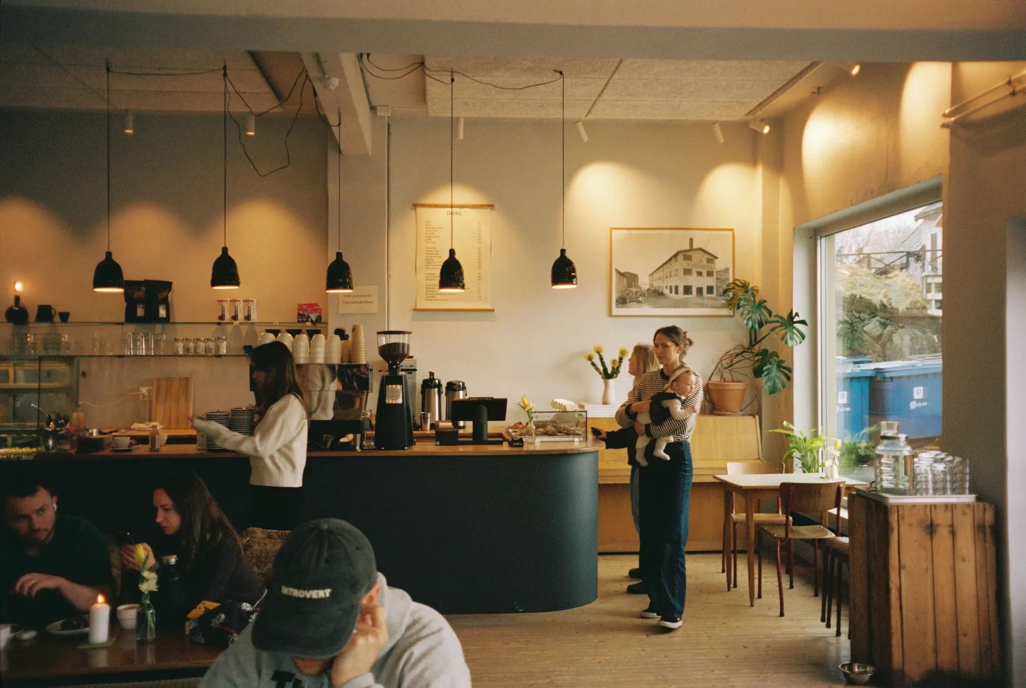 A café with a barista at the counter and harbour light through the window.
