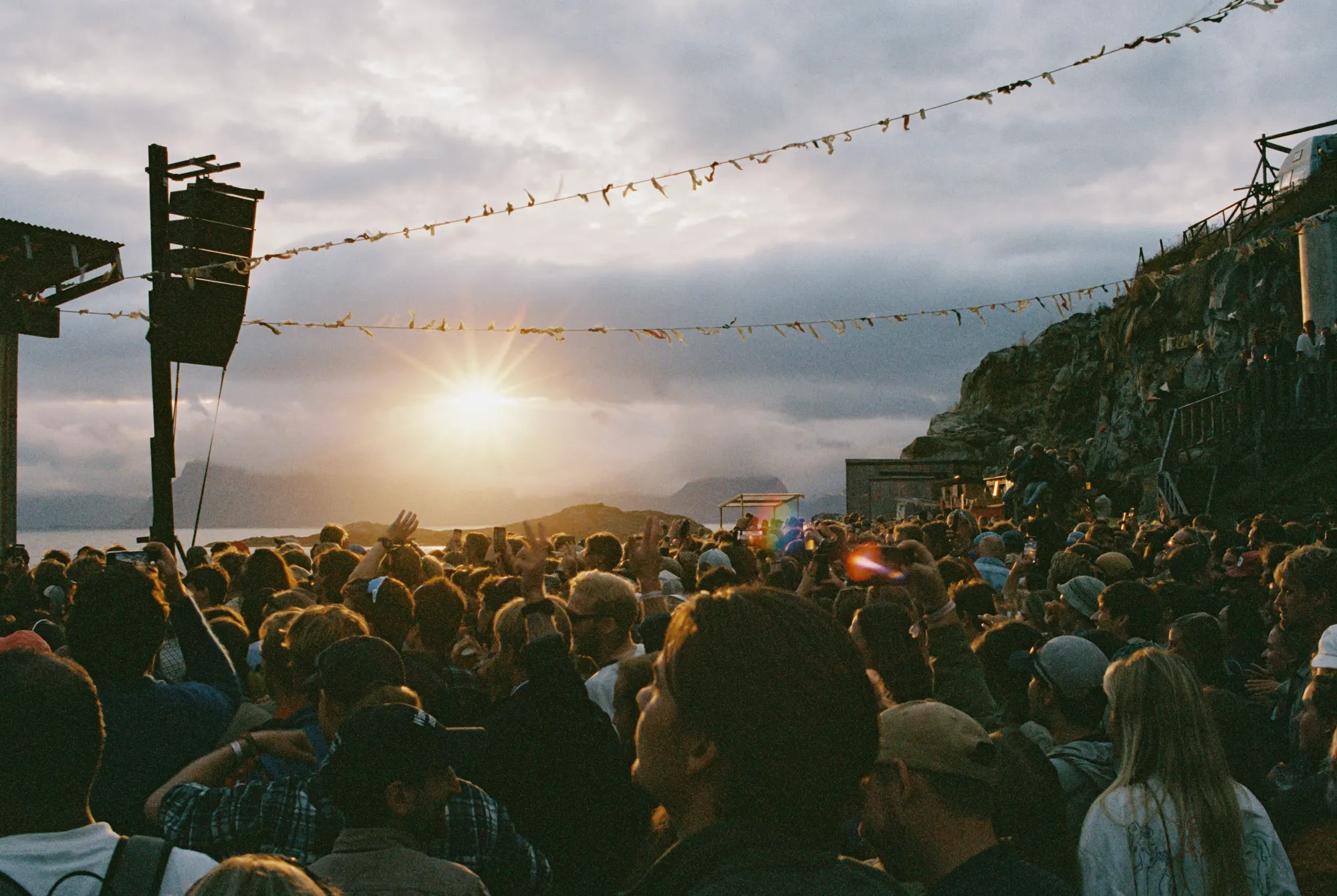 A crowd at an outdoor concert under the midnight sun