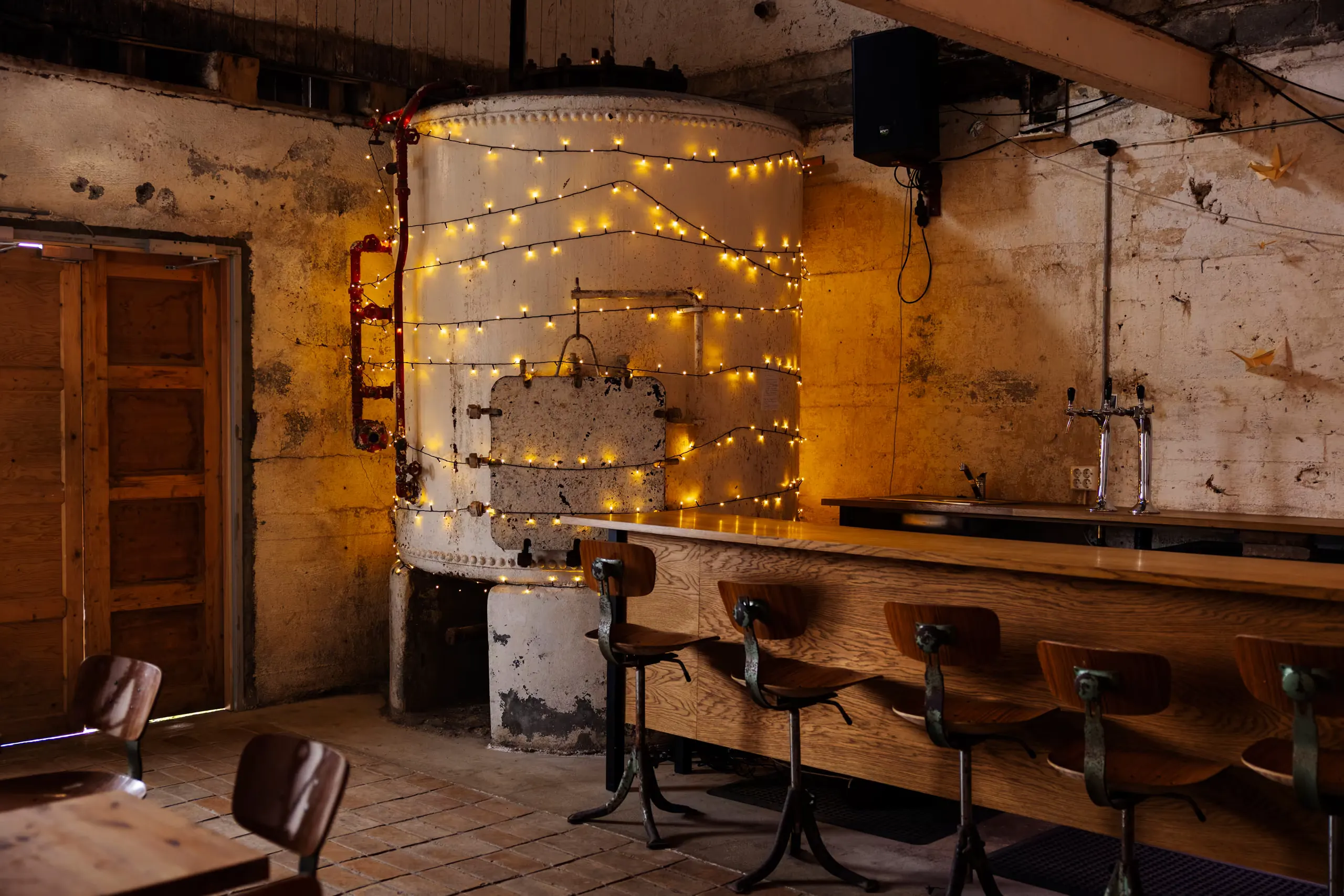 A bar counter with stools and string lights in a former factory