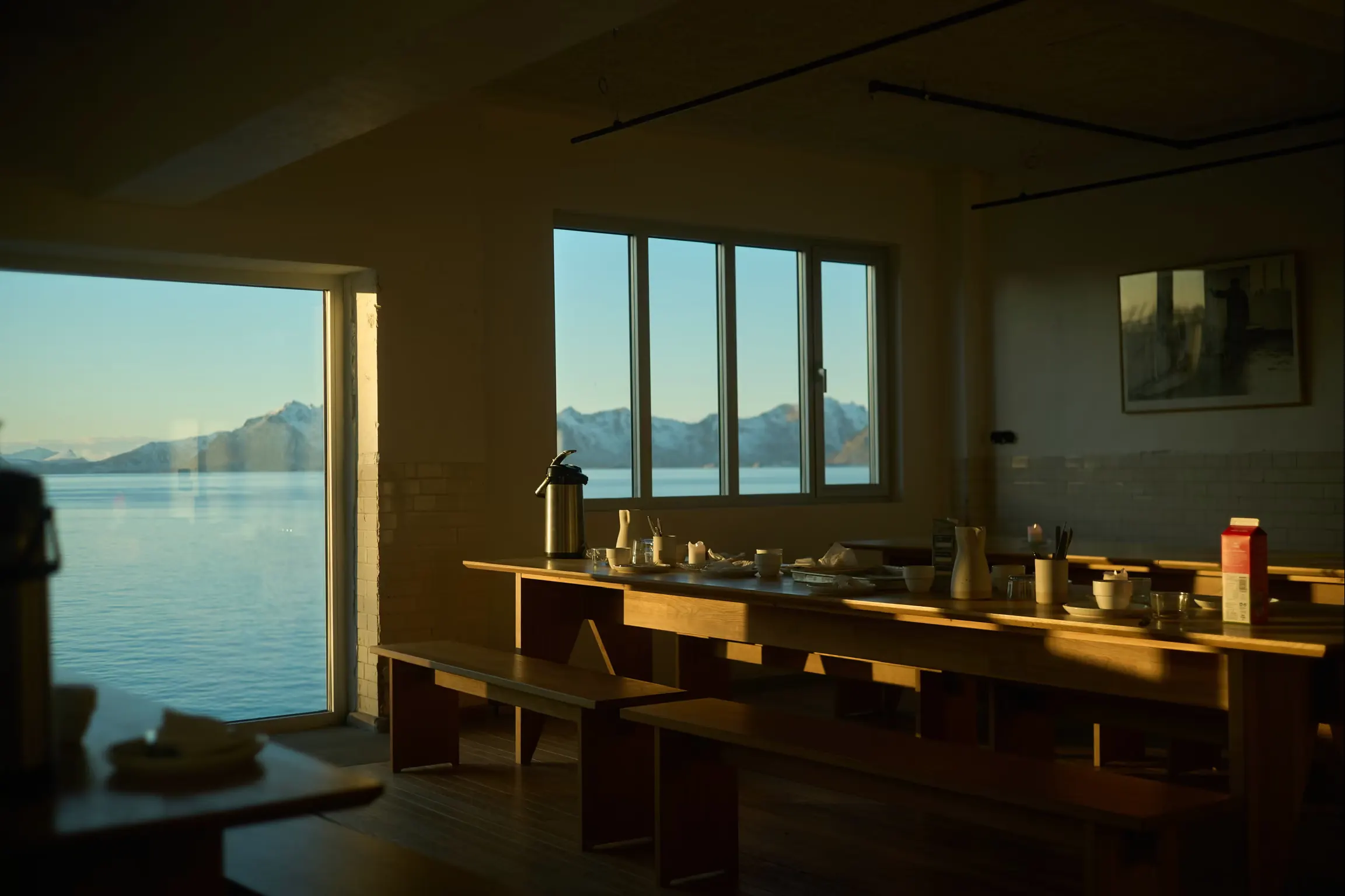 A dining room with long tables and windows onto the sea