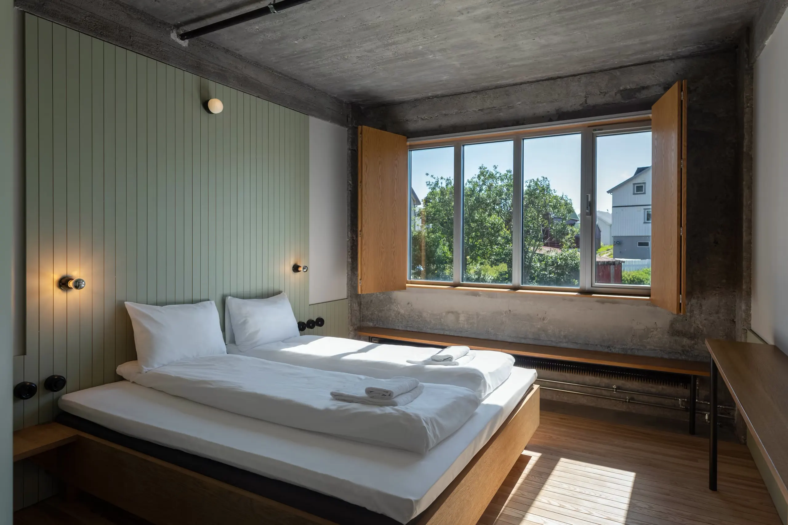 A hotel room with a made bed and a big window onto a garden